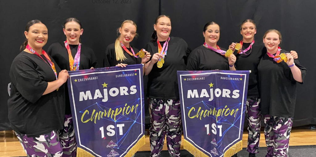 A photo of 7 senior dance students holding medals and winner banners